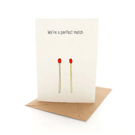 A greeting card with a white background, featuring a cartoon illustration of two red candles and the text 'We're a perfect match' in bold black letters.