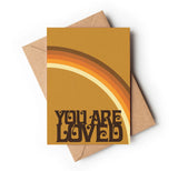 A greeting card with a brown envelope and a gradient of orange, yellow, and brown colors, ending with the text 'You are loved' in a bold, black font.