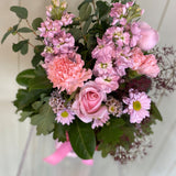 The PETITE BLOSSOM FUSS POT by Smellies Flowers features pastel roses, carnations, daisies, and greenery in a vibrant arrangement against a light backdrop, all sourced from Australian flower farms.