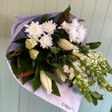 Bouquet of white flowers including snapdragons, lilies and chrysanthemums against a light green panelled wall