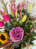 Bouquet of flowers with purple flower, sunflower, and green leaves.