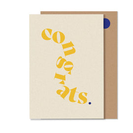 A yellow greeting card with the word 'CONGRATS' in bold, black letters, accompanied by a smaller dot. The card is placed in front of a brown envelope.