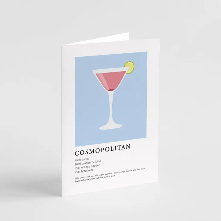 A greeting card featuring an illustration of a Cosmopolitan cocktail glass with a blue background. The card is set against a white backdrop, presenting a clean and simple aesthetic.