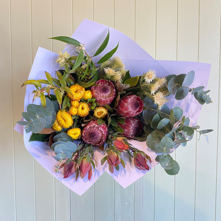 Bouquet of flowers with proteas and yellow strawflowers on a light wooden background