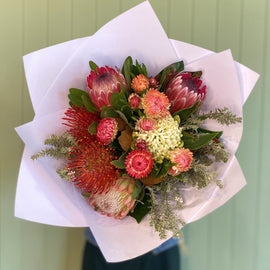 Bouquet of flowers wrapped in white paper against a green door.