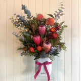 Bouquet of flowers with a pink ribbon in a clear container on a light wooden background