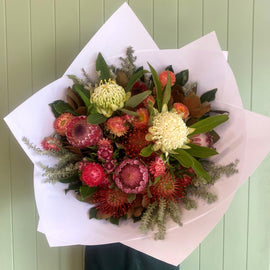 Bouquet of flowers wrapped in white paper against a light green wooden background