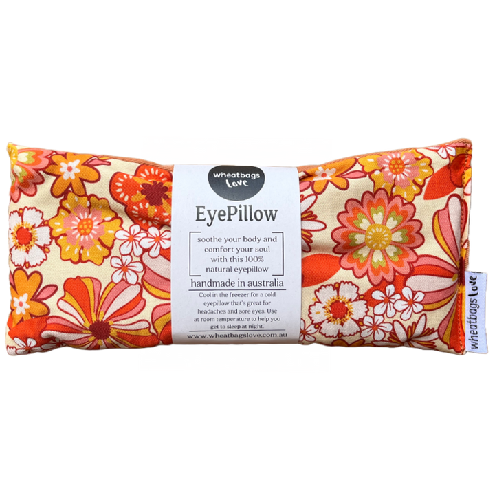 A rectangular eye pillow with a vibrant floral pattern in shades of orange and yellow, featuring product information and branding on a label.