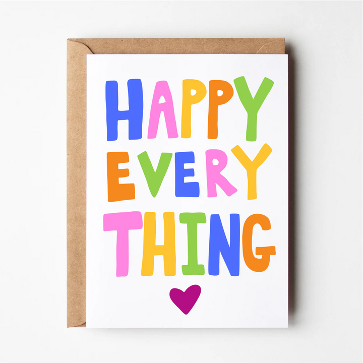 A colorful greeting card with the text 'HAPPY EVERYTHING' on it, placed on a card holder.