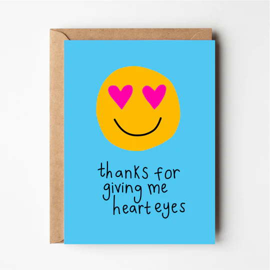 A blue greeting card with a smiley face and the phrase 'THANKS FOR GIVING ME HEART EYES' printed on it.