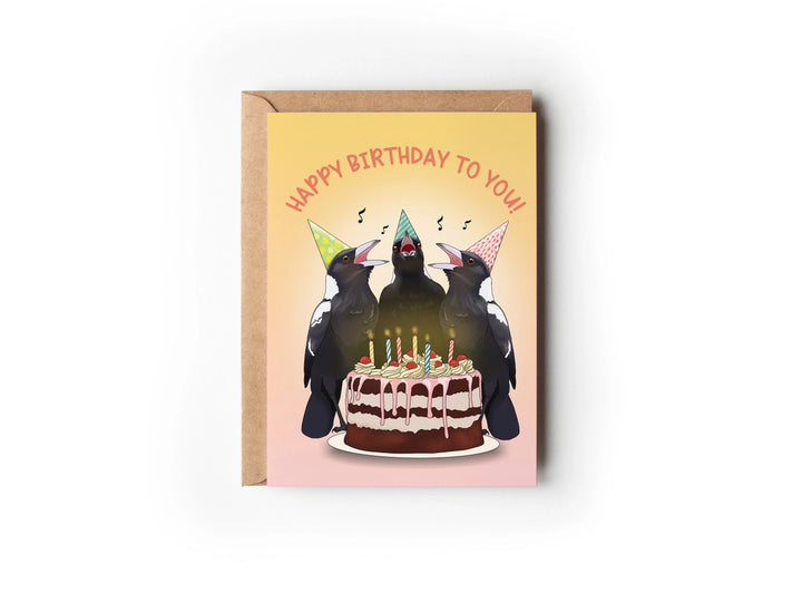 A greeting card with a yellow background featuring an illustration of a magpies wearing party hats singing around a birthday cake a with the text 'Happy Birthday To You!'.