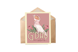 A greeting card featuring an illustration of a Major Mitchell cockatoo with protea flowers, the card is pink with the text 'G'DAY' and a message area, presented with a brown envelope.