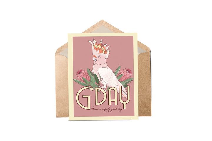 A greeting card featuring an illustration of a Major Mitchell cockatoo with protea flowers, the card is pink with the text 'G'DAY' and a message area, presented with a brown envelope.