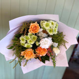 A bouquet of flowers including roses and other seasonal blooms in colors orange, white, green, and yellow, with foliage.