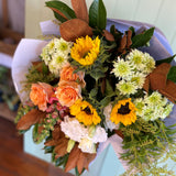 Bouquet of flowers in orange, yellow and green with magnolia leaf foliage wrapped in white paper
