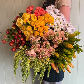 A bouquet of fresh flowers including shades of yellow, white, orange, and apricot with green foliage, wrapped and ready for gifting.