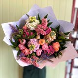Bouquet of colorful flowers wrapped in white paper against a light green wall.