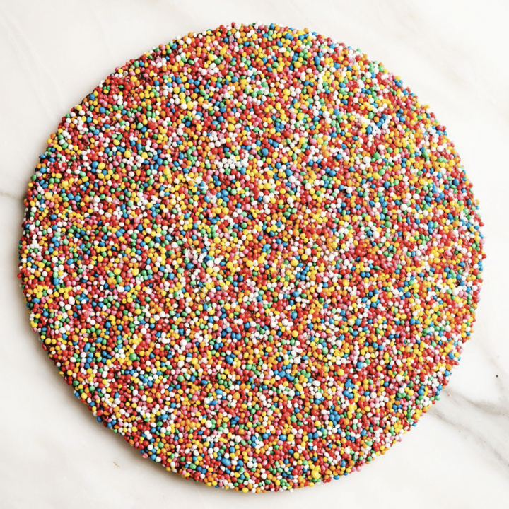 Round chocolate covered in multicolored sprinkles on a marble surface
