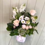 Small white vase filled with white flowers that includes snapdragons, roses, chrysanthemums, chincherinchees, strawflower and foliage.