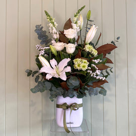 Floral arrangement in a white jar with a green ribbon against a wooden panel background