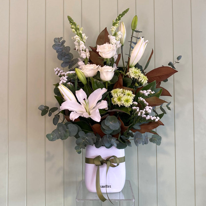 Floral arrangement in a white jar with a green ribbon against a wooden panel background