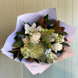 Bouquet of flowers wrapped in white paper against a light wooden panel background