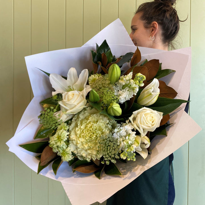 Person holding a bouquet of white flowers against a light green wall