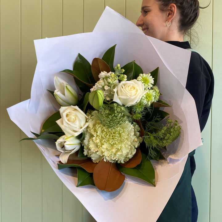 Person holding a bouquet of flowers wrapped in white paper against a light green background