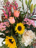 Bouquet of flowers with sunflowers and pink tulips against a white wall.
