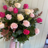 Close up photo of roses in pink, hot pink and cream with foliage against a panelled wall
