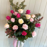 Pink vase holding a bouquet of pink and white roses and foliage against a panelled wall