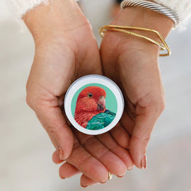 A person holding a Native Honeysuckle mini candle with artwork of a rosella bird on the label.
