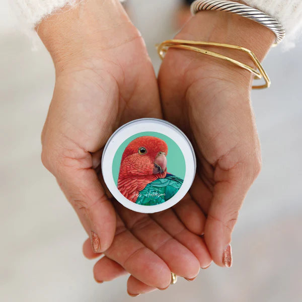 A person holding a Native Honeysuckle mini candle with artwork of a rosella bird on the label.