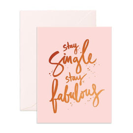This image features a charming greeting card with a soft pink background. The card displays the empowering message "STAY SINGLE STAY FABULOUS" in elegant, scripted lettering in a combination of gold and brown tones, adding a stylish touch to the design.