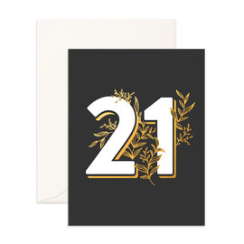 The Fox and Fallow 21 Greeting Card features a black cover with the number "21" prominently displayed in large white and gold lettering, accented with gold floral designs. A plain white envelope is partially visible behind the card, ready for your personal message.