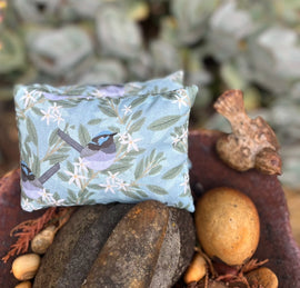 Small decorative pillow with bird and floral pattern on stones and plants