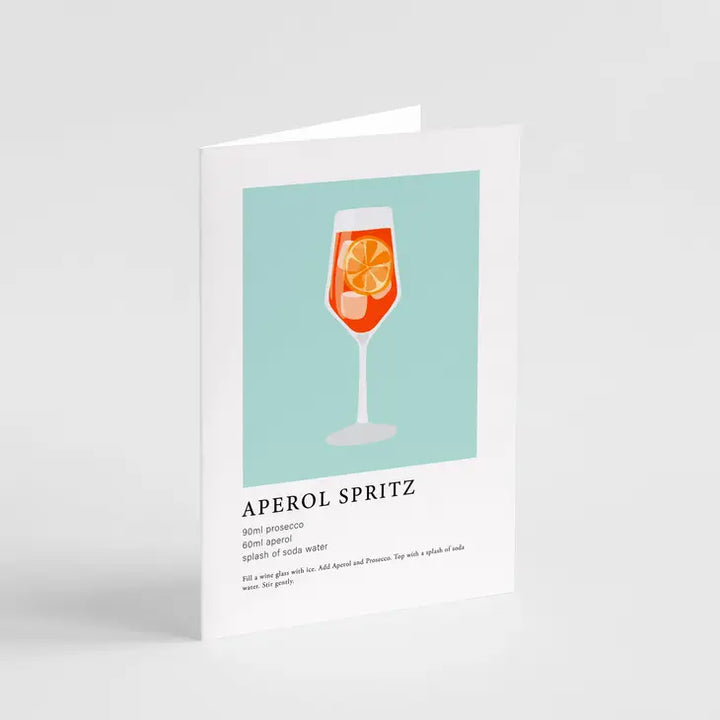 An image of the APEROL SPRITZ GREETING CARD by Popsy Press showcases a minimalist illustration of an Aperol Spritz cocktail. The card depicts a glass filled with an orange drink, garnished with citrus slices. Below the image, ideal for Valentine's Day, a recipe for making an Aperol Spritz is printed.