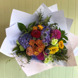 Bouquet of colorful flowers wrapped in white paper against a light green wall.