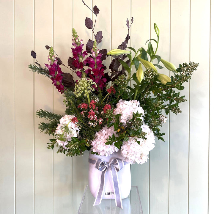 White vase of flowers in a white vase with a pink ribbon against a light wooden panel background
