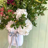White vase of flowers with a white container against a light green background