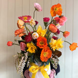 Vase of colorful flowers with a yellow ribbon in front of a white curtain