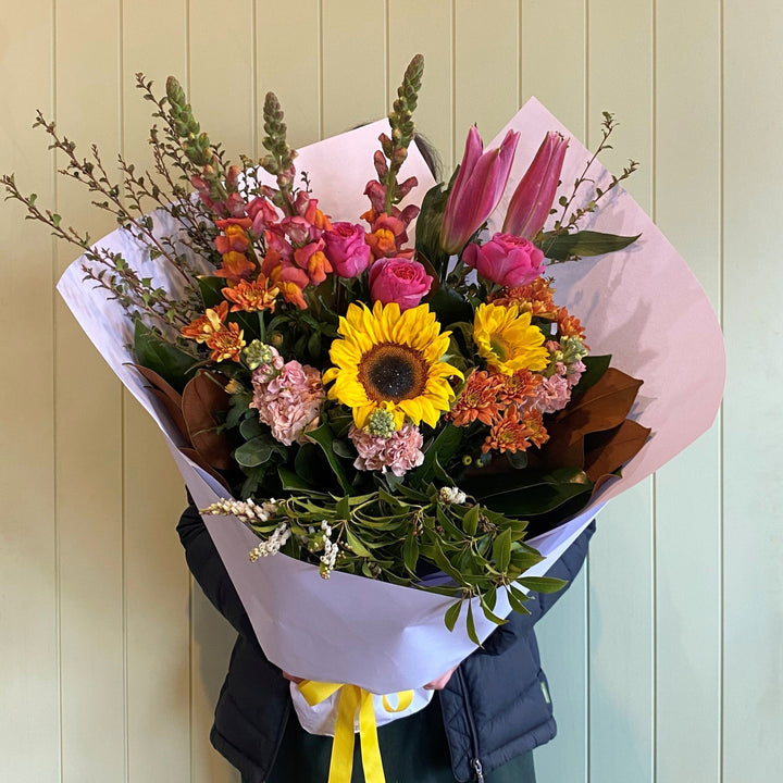 Bouquet of colorful flowers with a yellow ribbon against a light wooden panel background