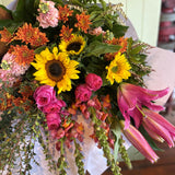 Bouquet of colorful flowers including sunflowers and pink roses on a white surface.