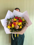 Person holding a bouquet of colorful flowers against a light green wall.