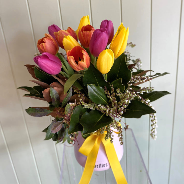 Vase of colorful tulips with a yellow ribbon against a white wooden panel background