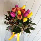Vase of colorful tulips with a yellow ribbon against a white wooden background