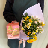 Person wearing a 'smellies' apron holding a bouquet of flowers and a box.