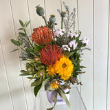 Bouquet of flowers with red proteas, yellow daisies, and greenery on a white background