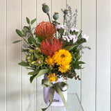Bouquet of flowers in a white vase on a clear stand against a light wooden panel background