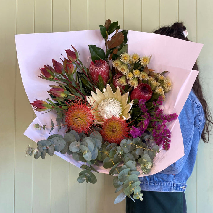 Bouquet of colorful flowers held by a person against a light green wall.